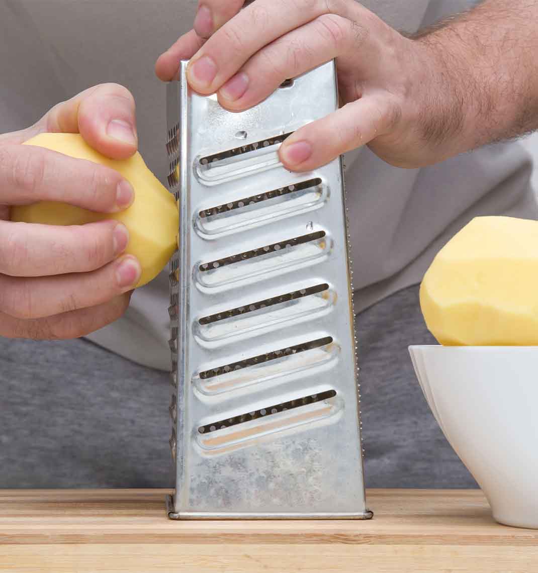Hands grating a peeled potato on a box grater