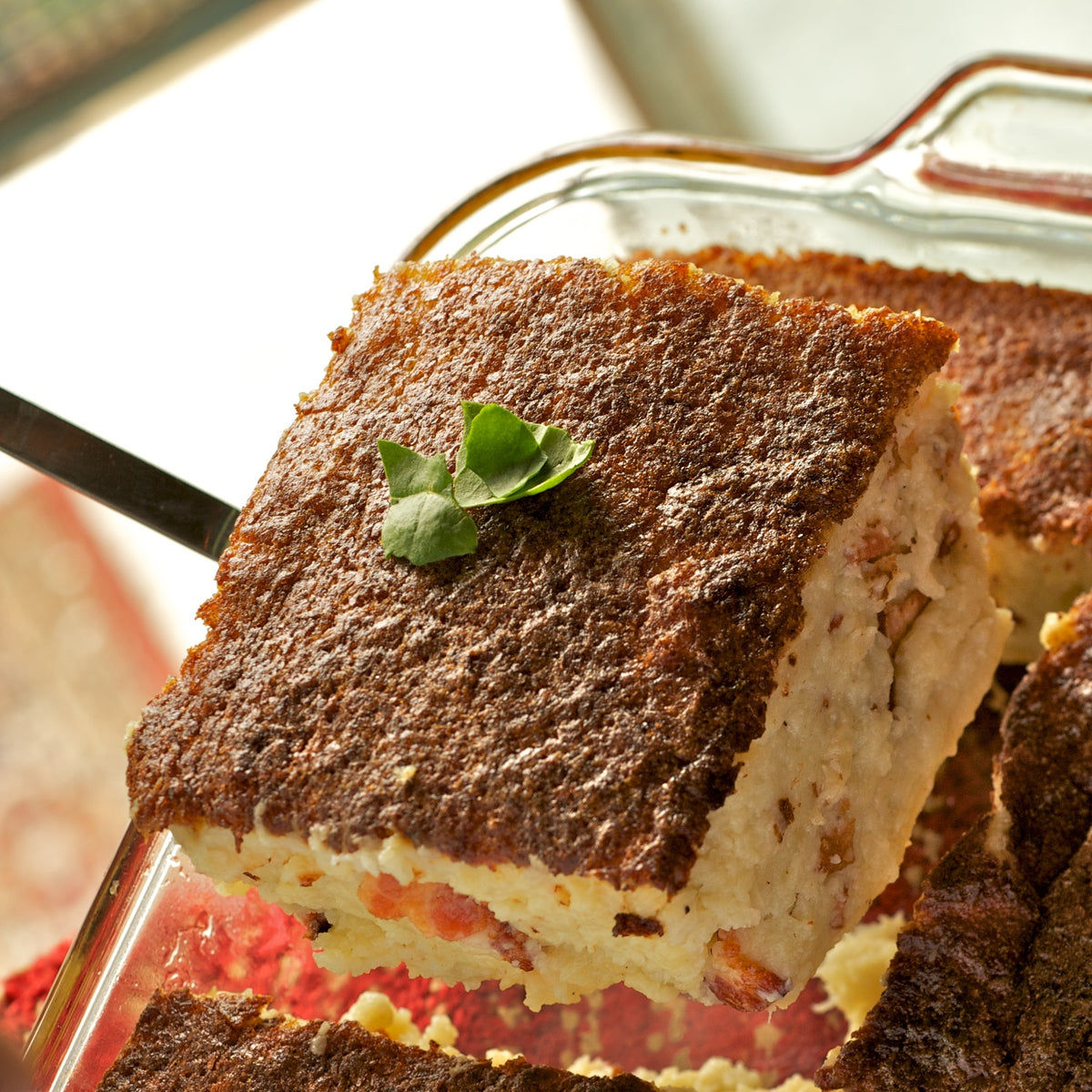 A square of Grandma Ann’s kugelis with its golden-brown crust, lifted from a glass baking dish